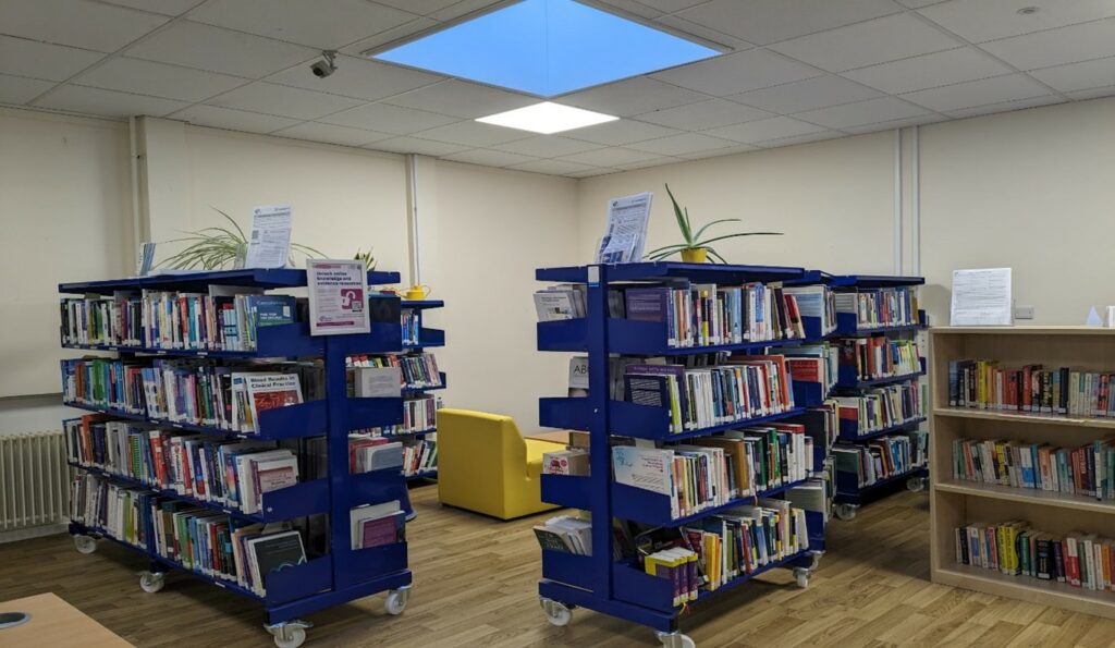 A library with blue stacks filled with books, yellow armchair seating and a wooden floor.