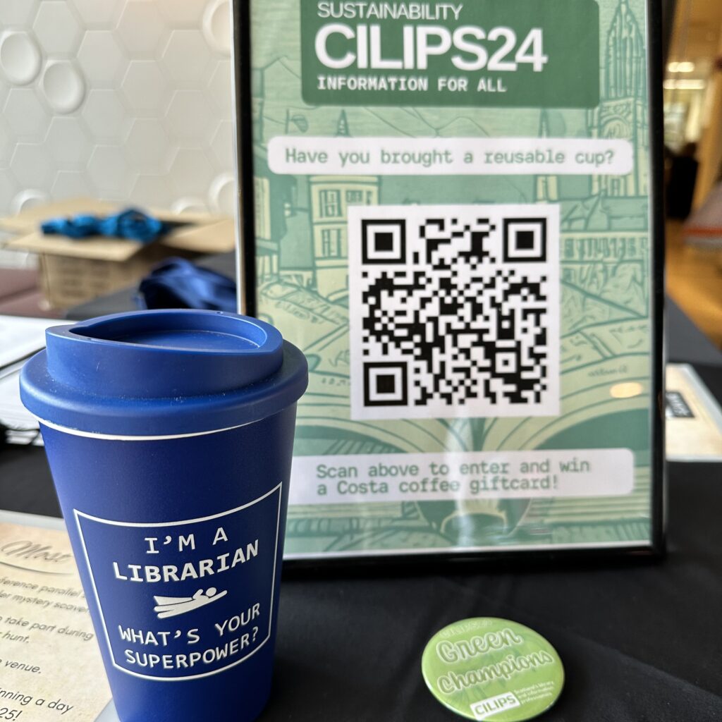 The CILIPS24 reusable coffee cup competition beside a Green Team pin badge and a coffee cup reading 'I'm a librarian. What's your superpower?'