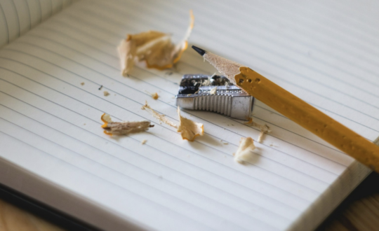 Image of pencil being sharpened on top of lined paper.